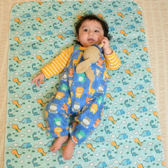 Baby lying on a Happy Matty dinosaur print bed protector mat